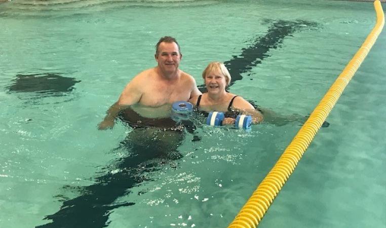 two people next to each other in the pool, one is holding water weights